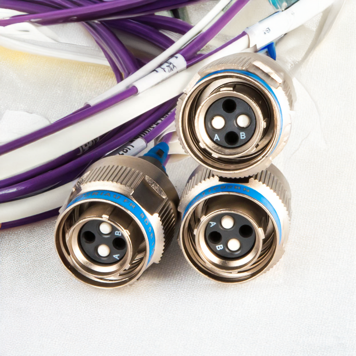 Three ruggedised fibre optic connectors with chrome bodies and blue bands, terminated to purple and white fibre cables